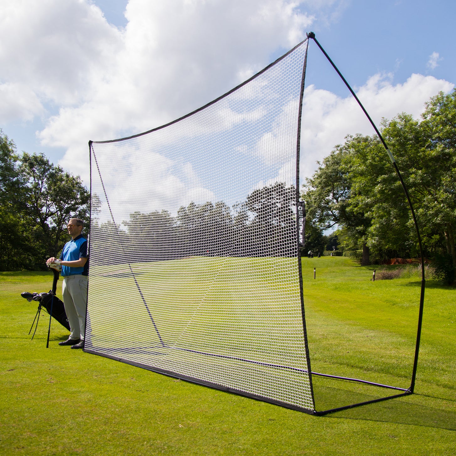 Golfer standing beside the MEGA NET Golf Hitting Net 12x9' set up on a golf course fairway, seen side on.
