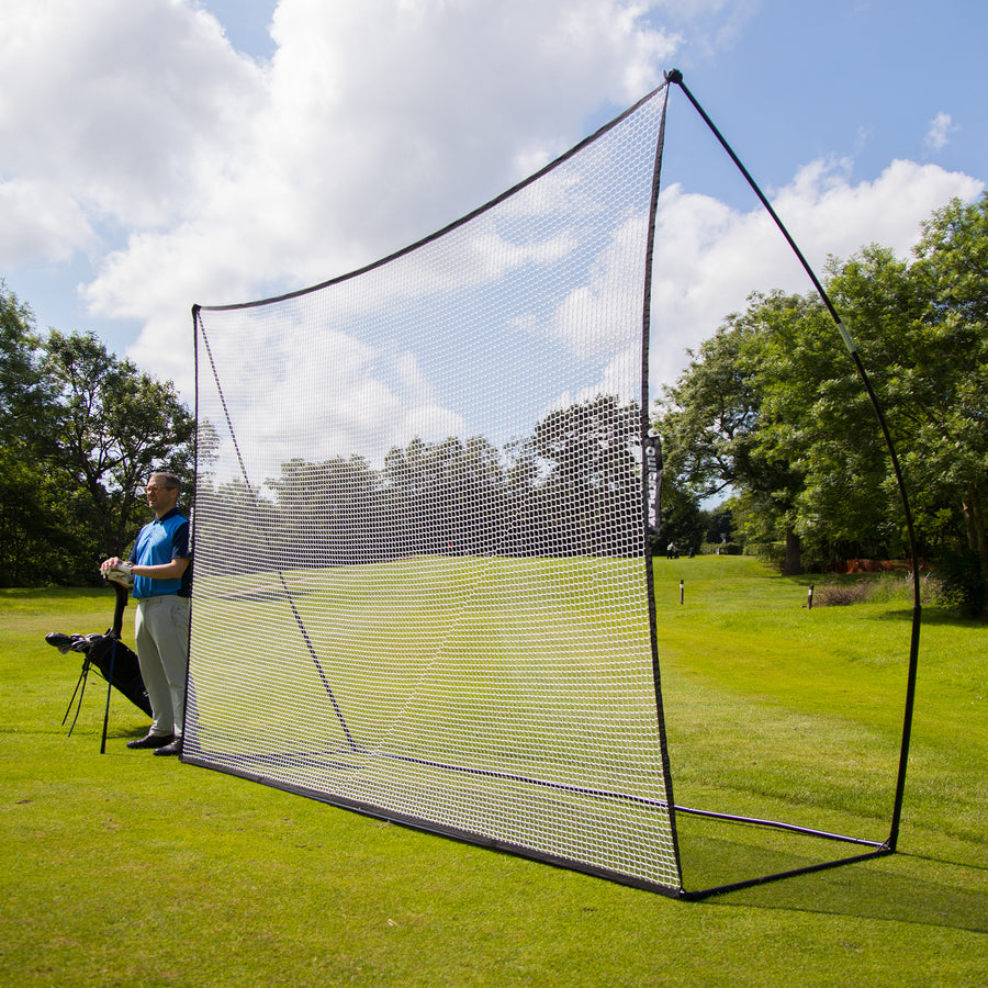Golfer standing beside the MEGA NET Golf Hitting Net 12x9' set up on a golf course fairway, seen side on.
