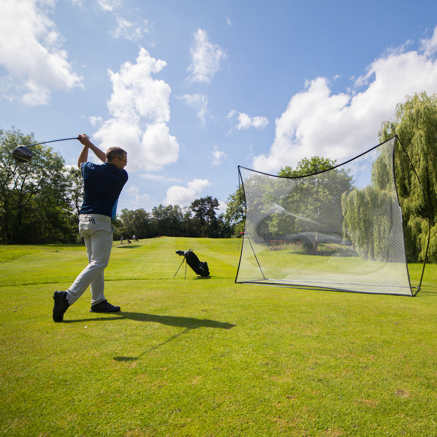 Golfer mid swing with a driver on a fairway, with the MEGA NET Golf Hitting Net 12x9' set up behind him.