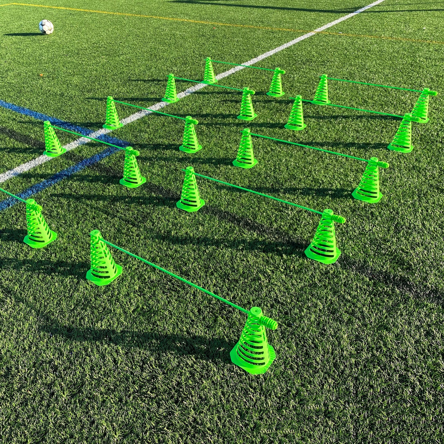 Green 9" collapsible cones and agility poles set out as rows of hurdles on an artificial pitch.