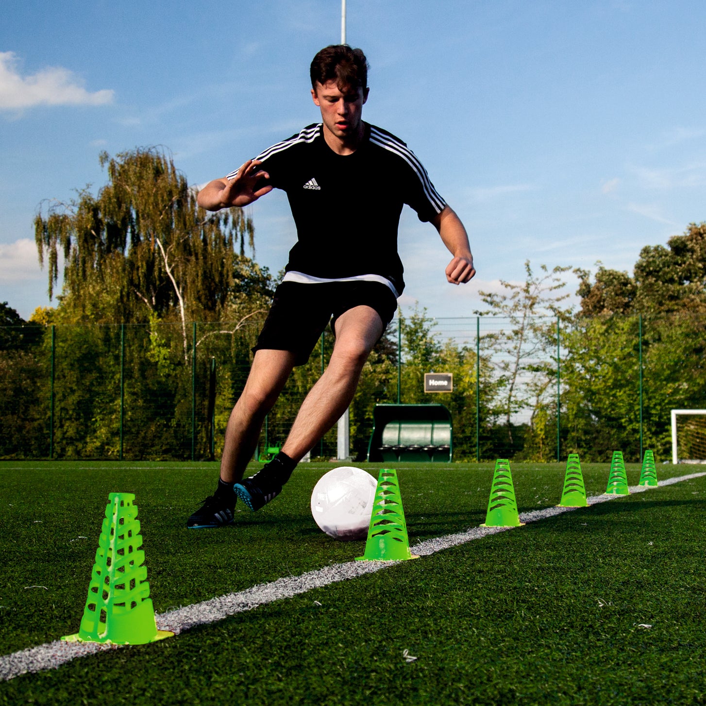 Player dribbling a ball through a line of green 9" collapsible cones on an artificial pitch.