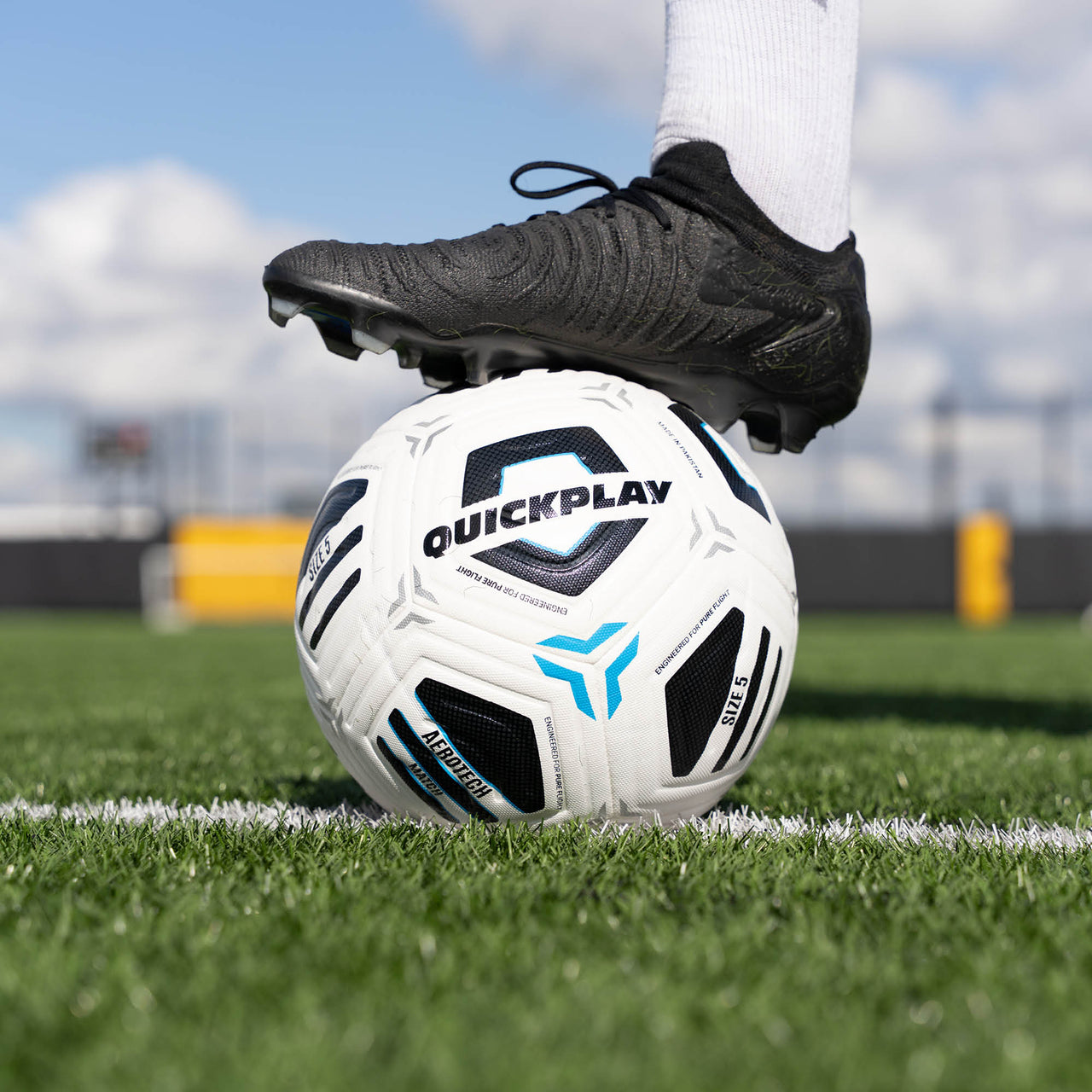 Football with 'QuickPlay' branding on a grass field, foot on top