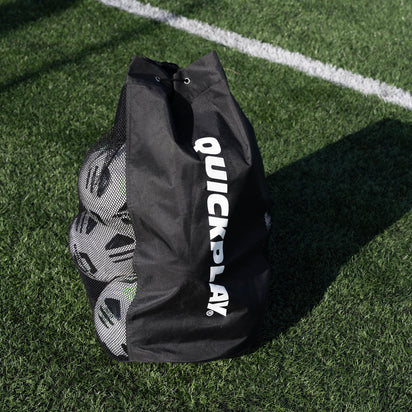 Black football bag with 'QuickPlay' branding on a grass field with football balls inside.