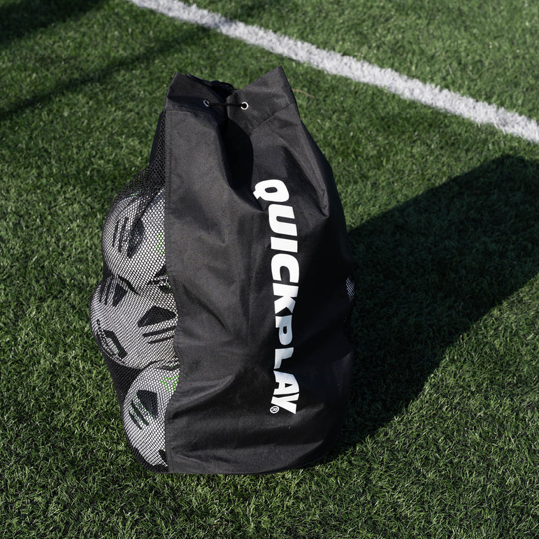 Black football bag with 'QuickPlay' branding on a grass field with football balls inside.