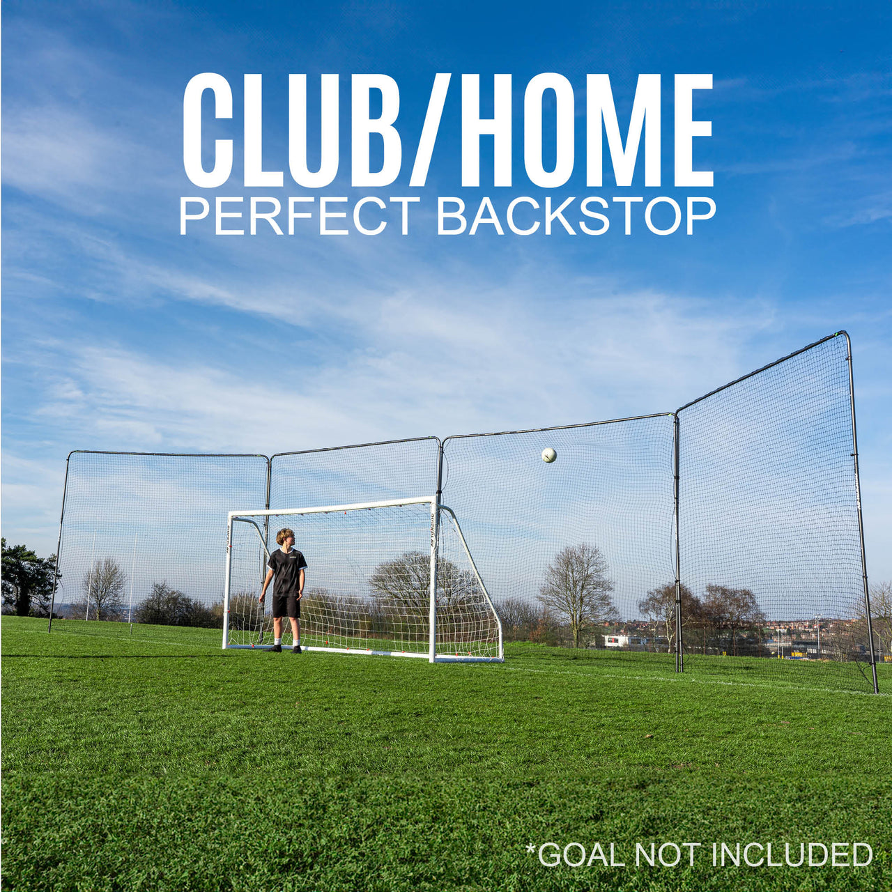football goal backstop with a barrier net system behind it on a grass field with a clear blue sky.