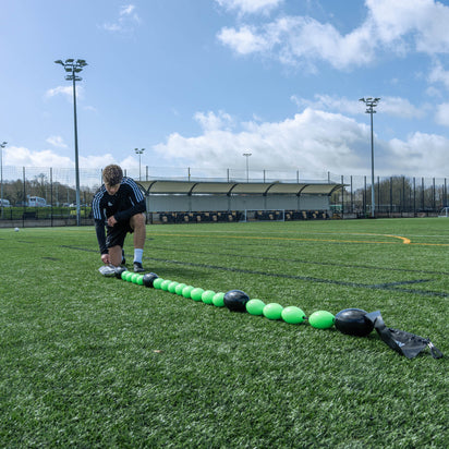 Person setting up a goalkeeper deflection line on a grass field with stadium in the background