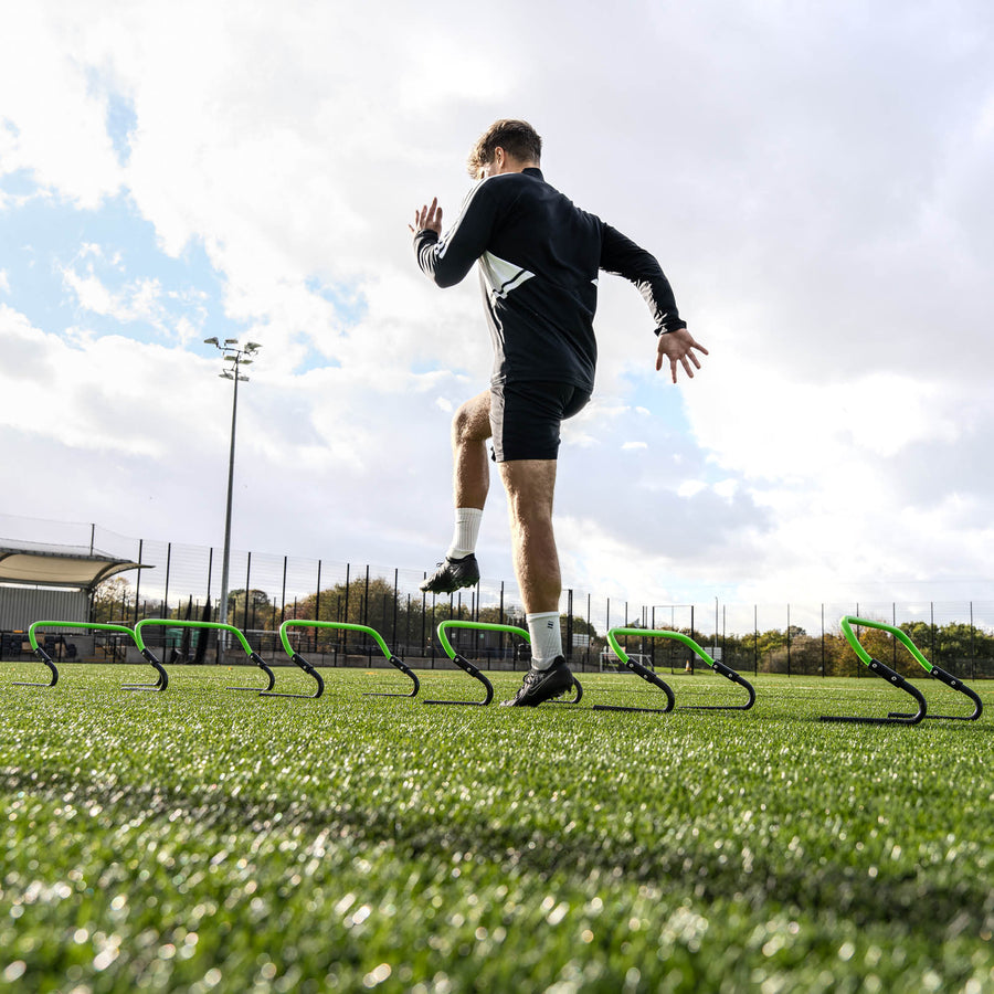 Person running on a sports field with green hurdles.