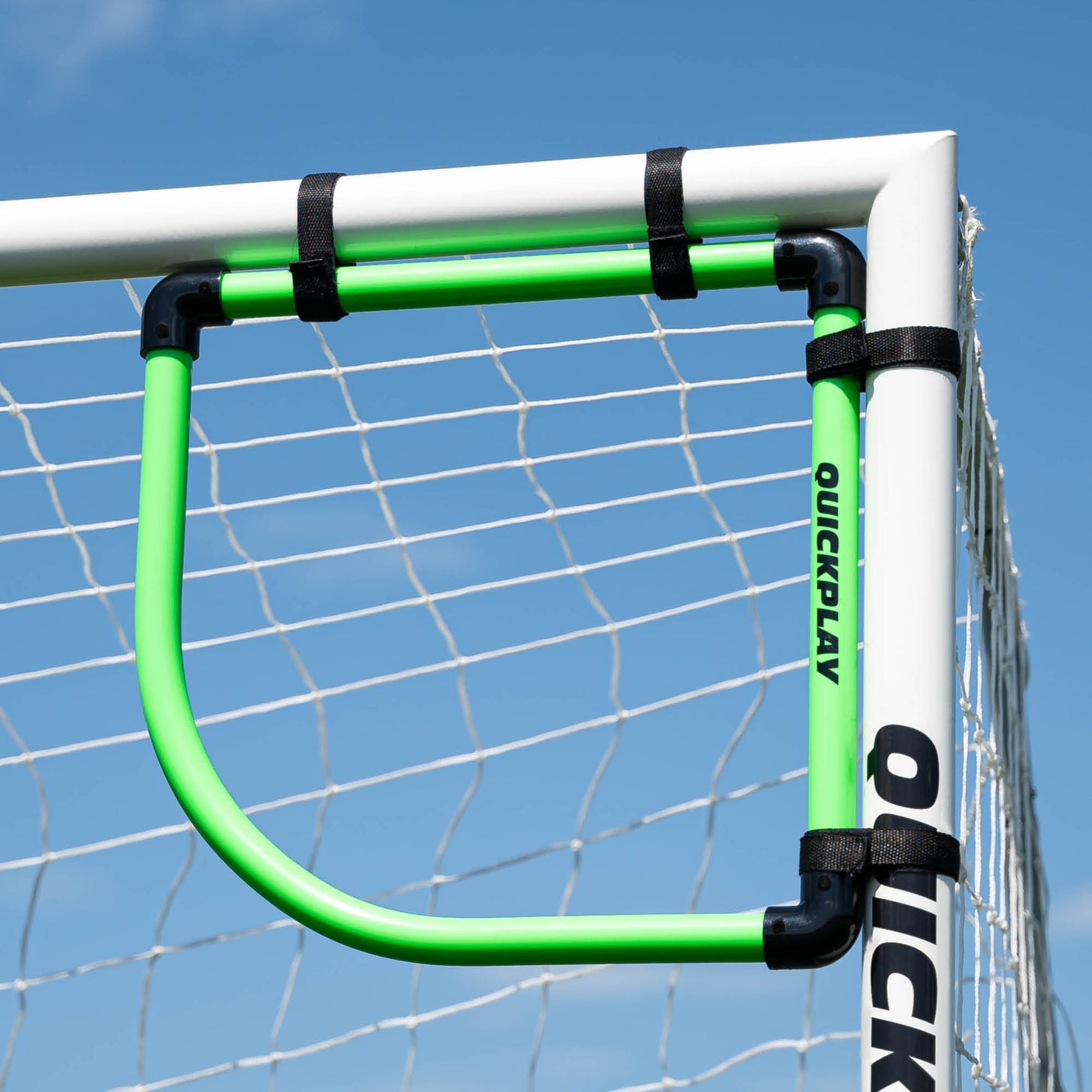 Green Goal Corner Target Frame strapped into the top corner of a white QUICKPLAY goal against a blue sky.