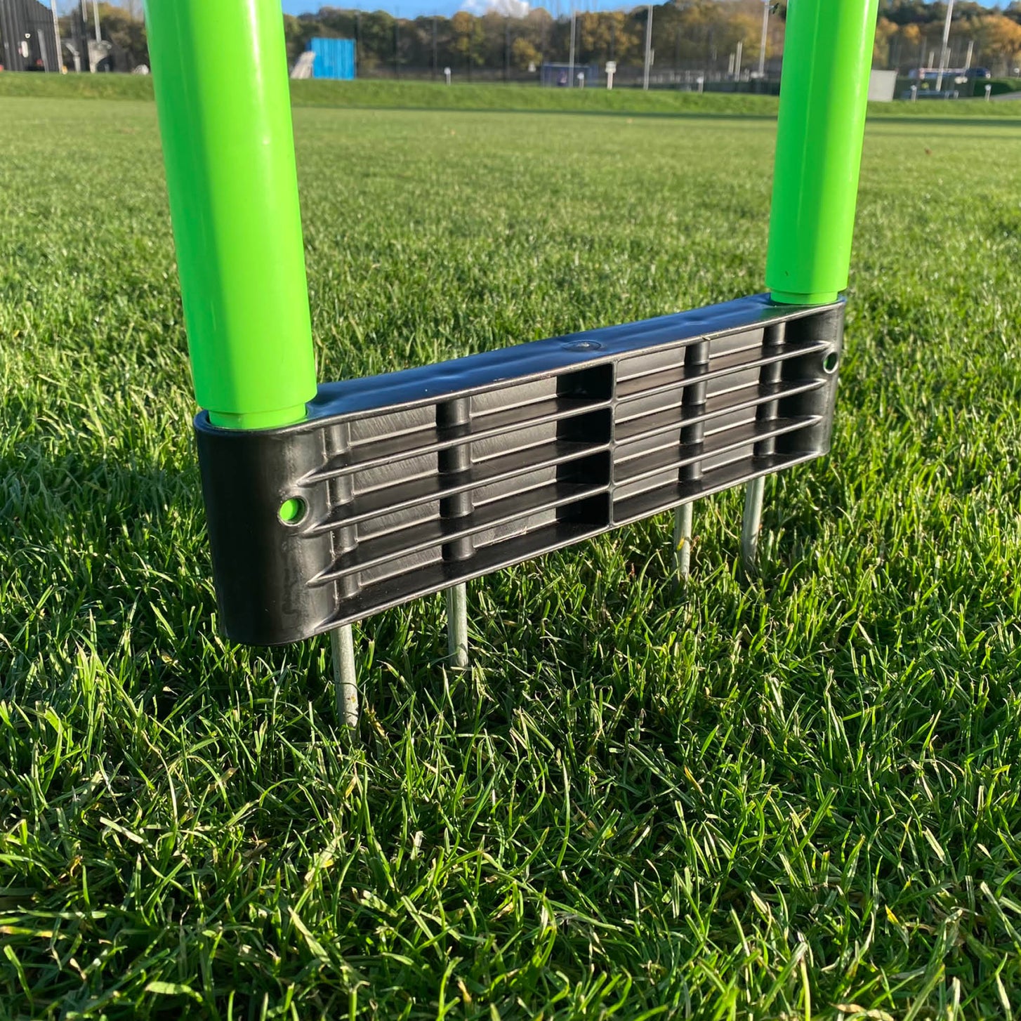 REPLAY Defender Mannequin close up of the black base with metal spikes pushed into a grass pitch, between the two green poles.