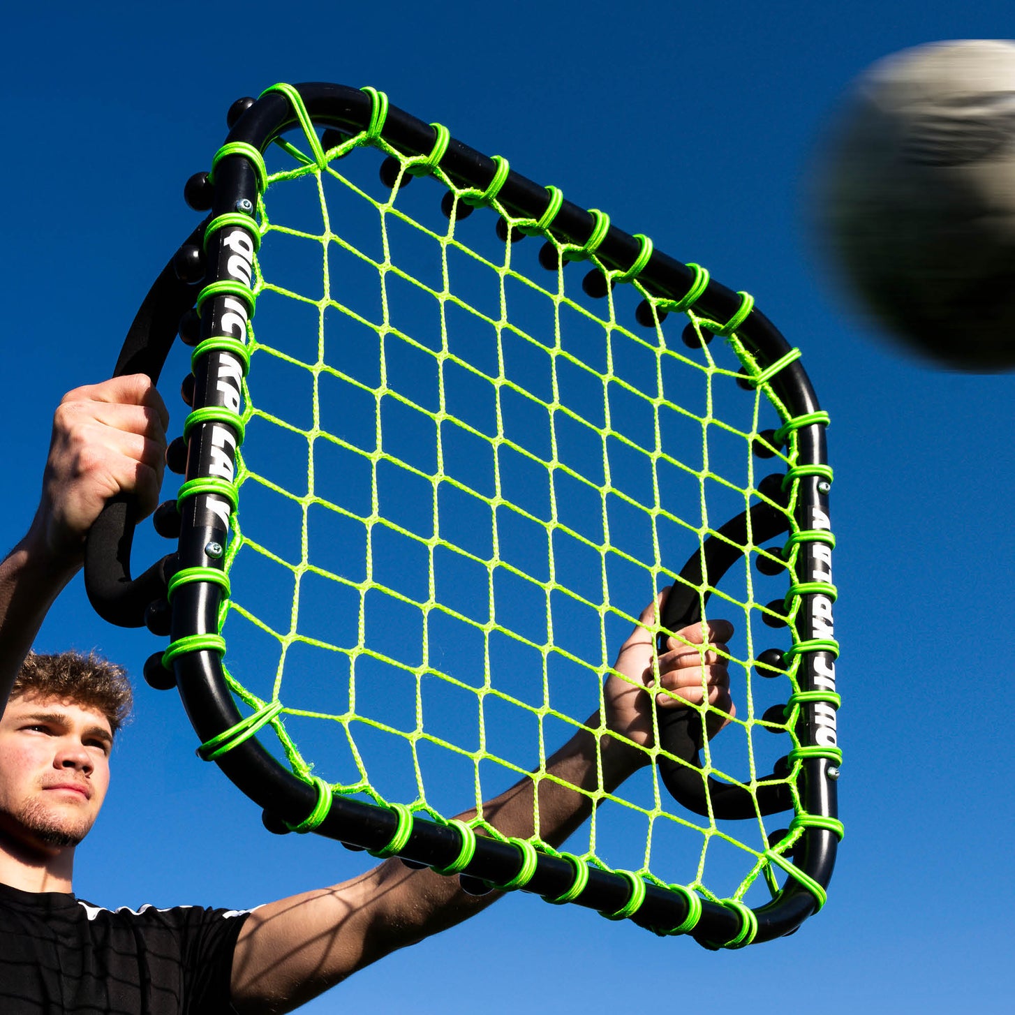 Player holding the Handheld Rebounder above his head against a blue sky as a ball flies towards the net.
