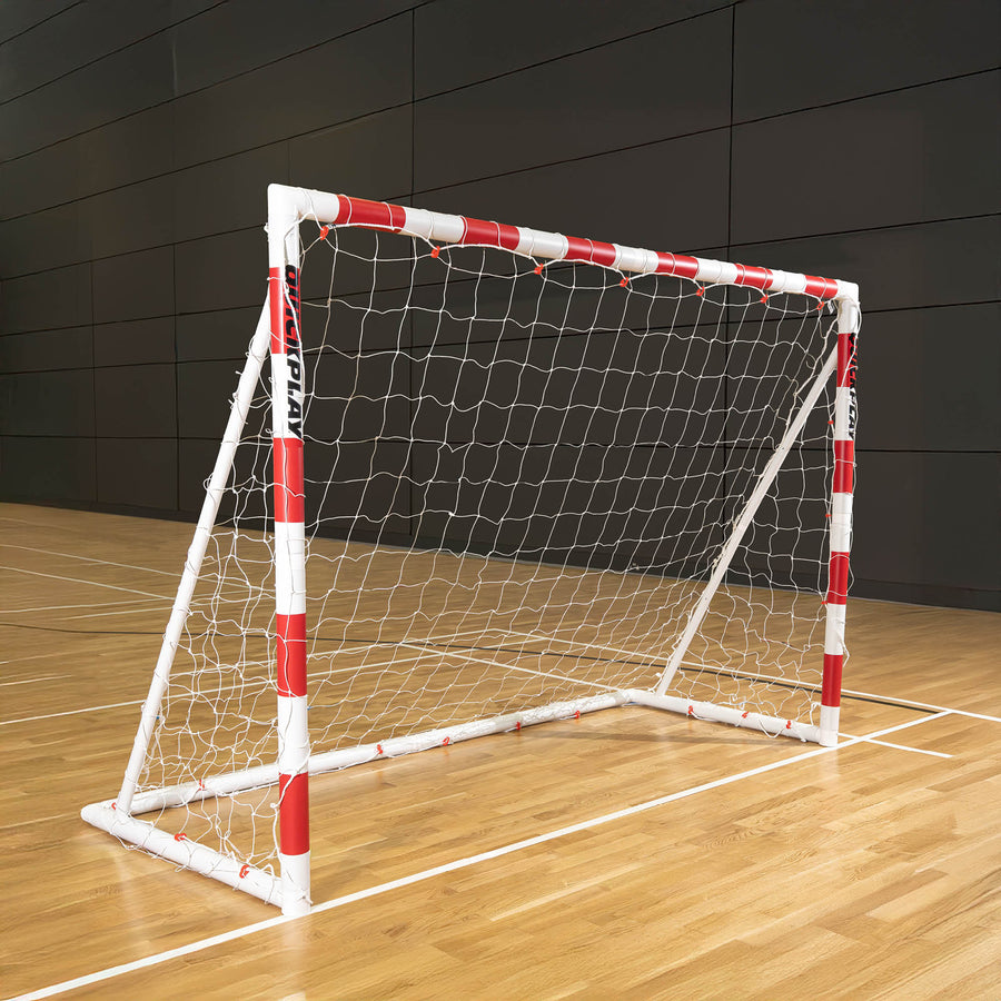Small handball goal with red and white frame on a wooden floor against a dark panelled wall.