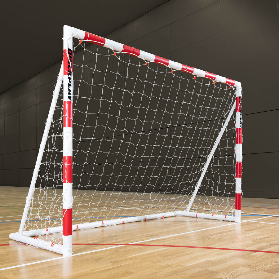 Small handball goal with red and white frame on a wooden floor against a dark wall.