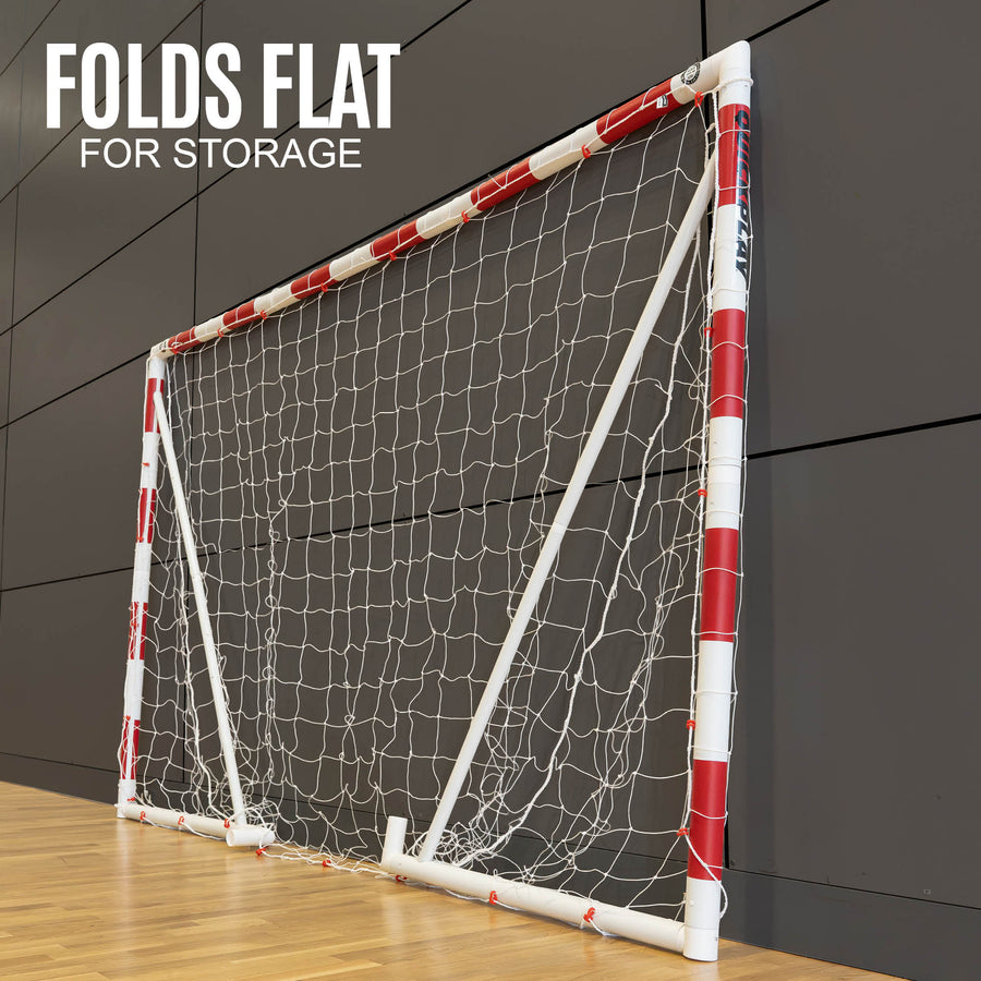 Portable handball goal with red and white design on a wooden floor against a dark panelled wall.