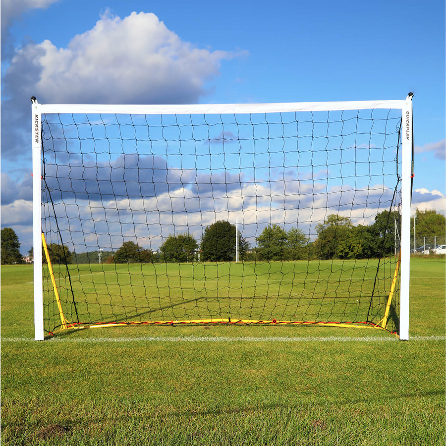 KICKSTER 8x5' goal front view with a white frame, yellow base and black net on a grass pitch under a cloudy sky.