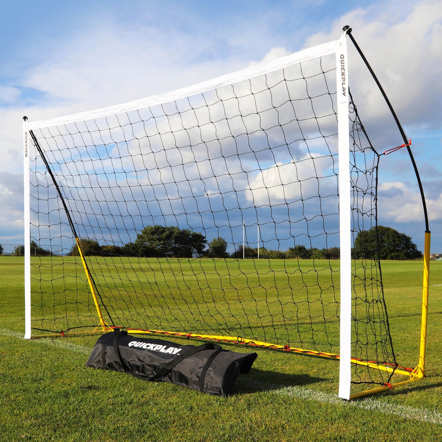 KICKSTER 8x5' goal with a white crossbar, yellow base frame and black net on grass, with its black QUICKPLAY bag in front.