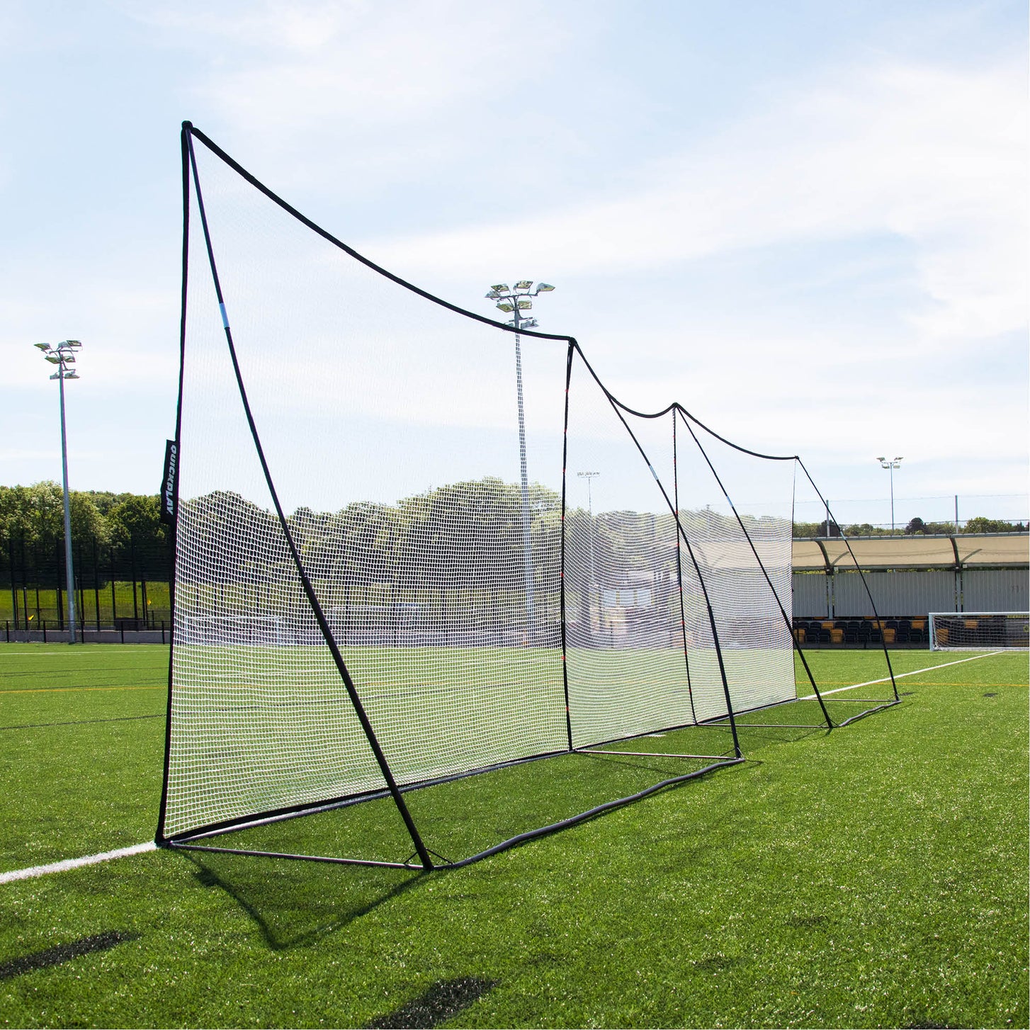 MEGA NET 12x9' ball-stop nets joined side by side in a long line along the edge of an artificial pitch.