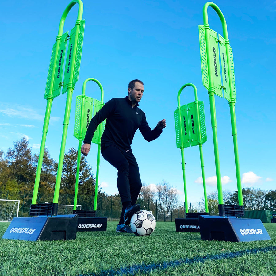 Low-angle view of a player with a ball among green mannequins standing in REPLAY Blocks under a blue sky.