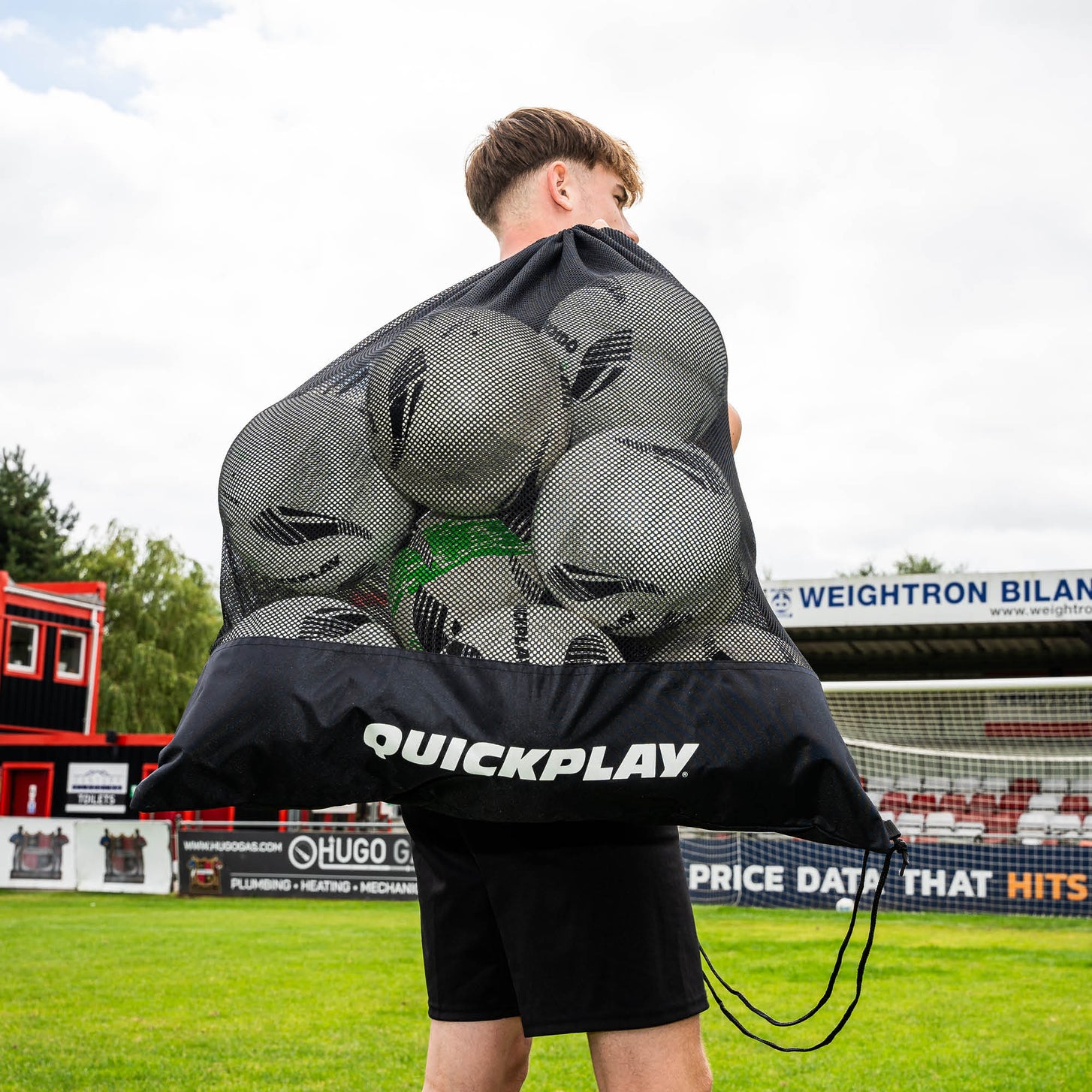 Player carrying the QUICKPLAY Mesh Football Bag full of footballs over his shoulder at a football ground.