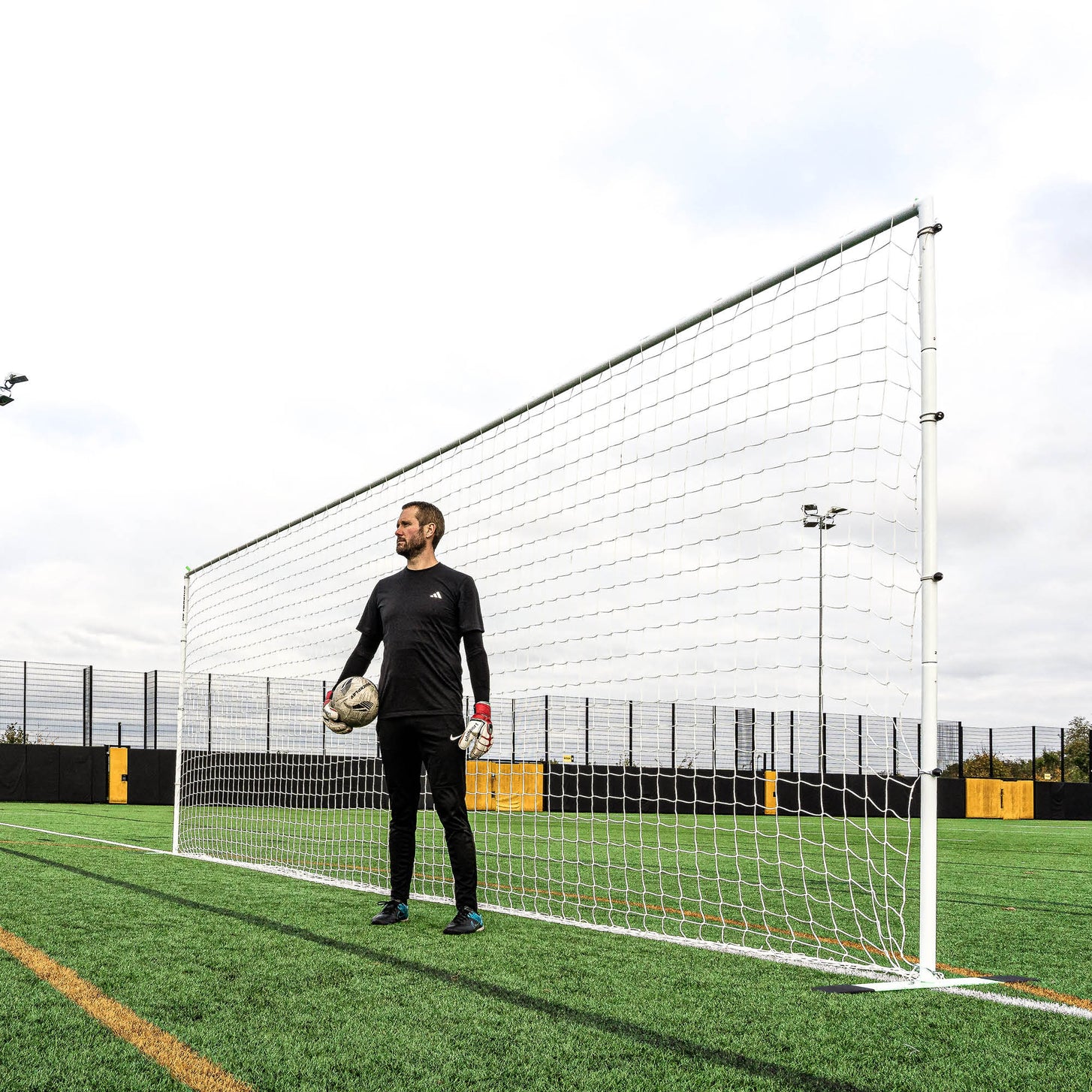 Goalkeeper holding a ball in front of the white PRO ALU Training Frame 18.5x6.5' on an artificial pitch.