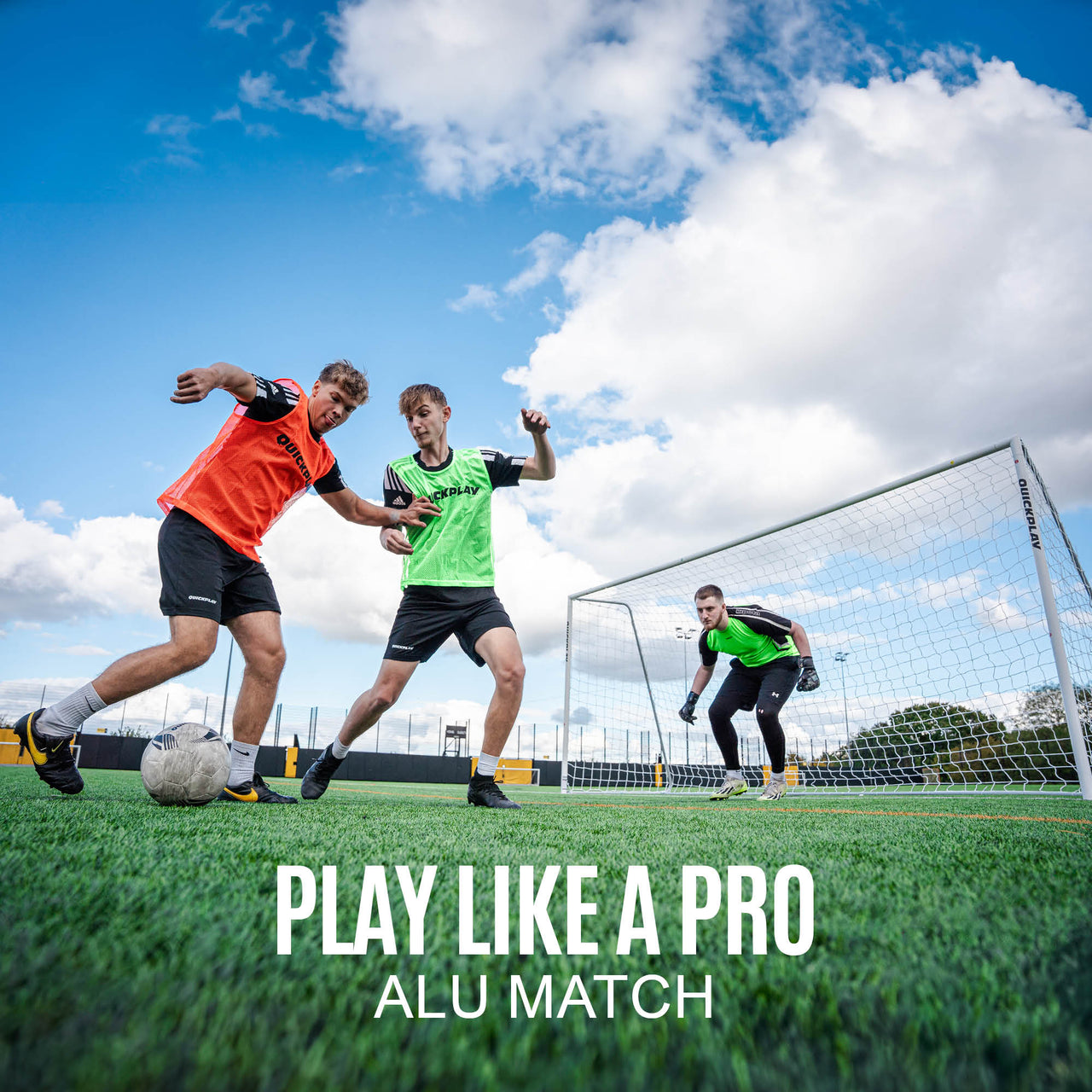 Two football players in action on a field with a goalkeeper, under a blue sky with clouds.