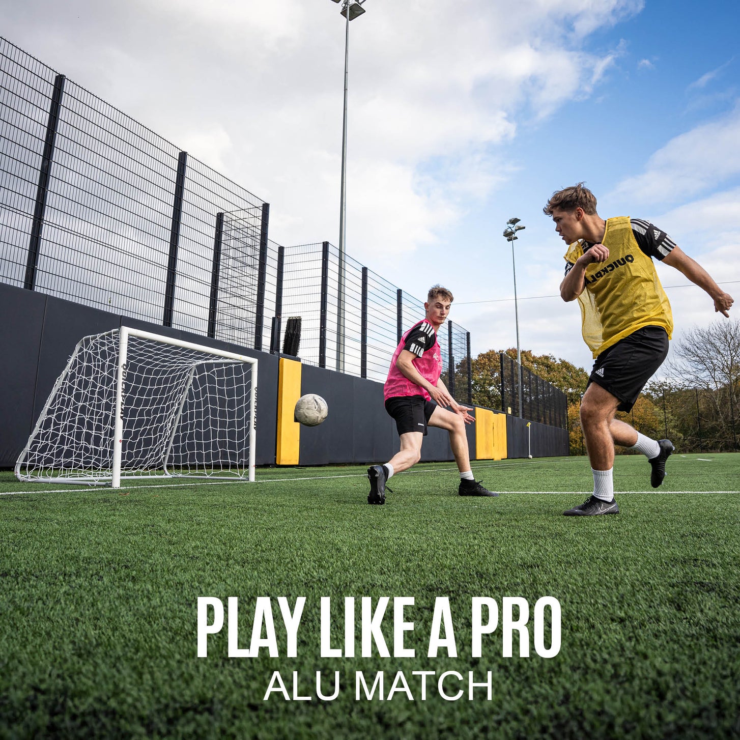 Players in bibs passing near the PRO ALU Match60 8x5' goal on a fenced artificial pitch, with the text "Play like a pro, ALU Match".