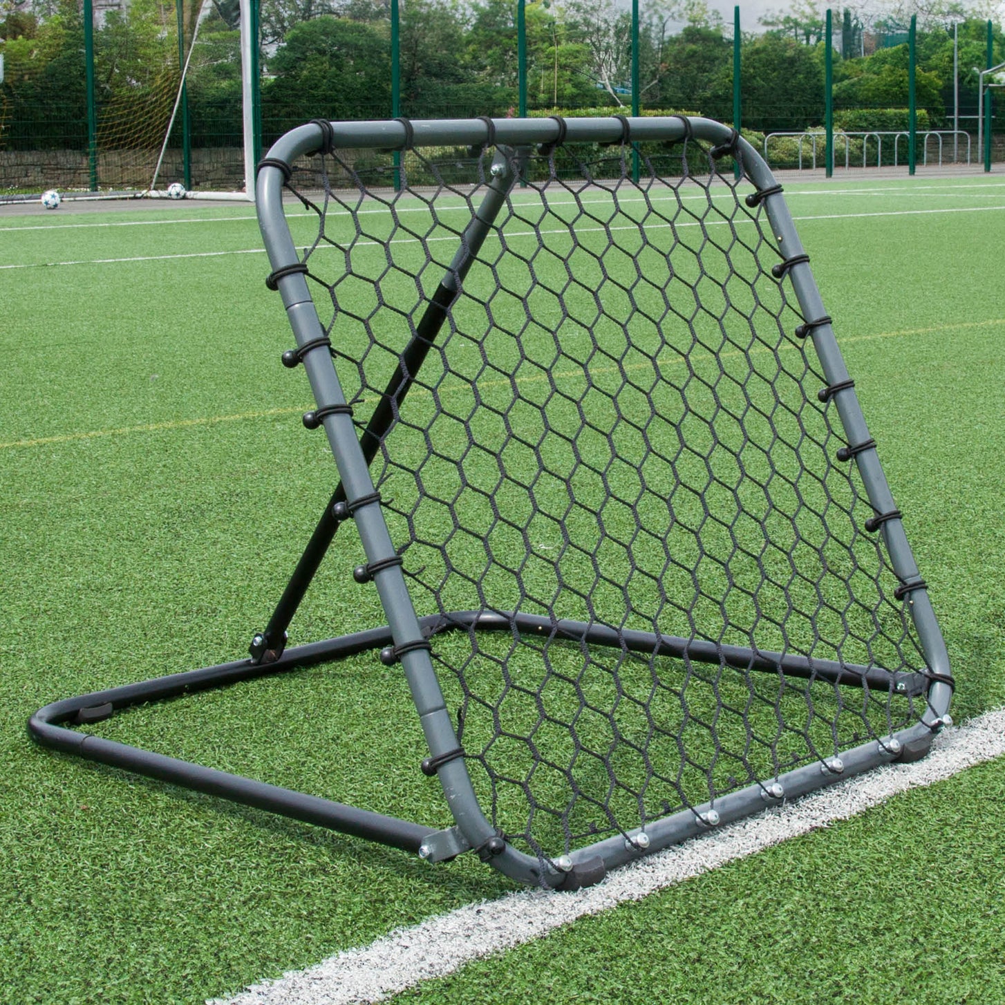 PRO Rebounder 3x3' with a grey frame and black hexagon net, standing at an angle on an artificial pitch.
