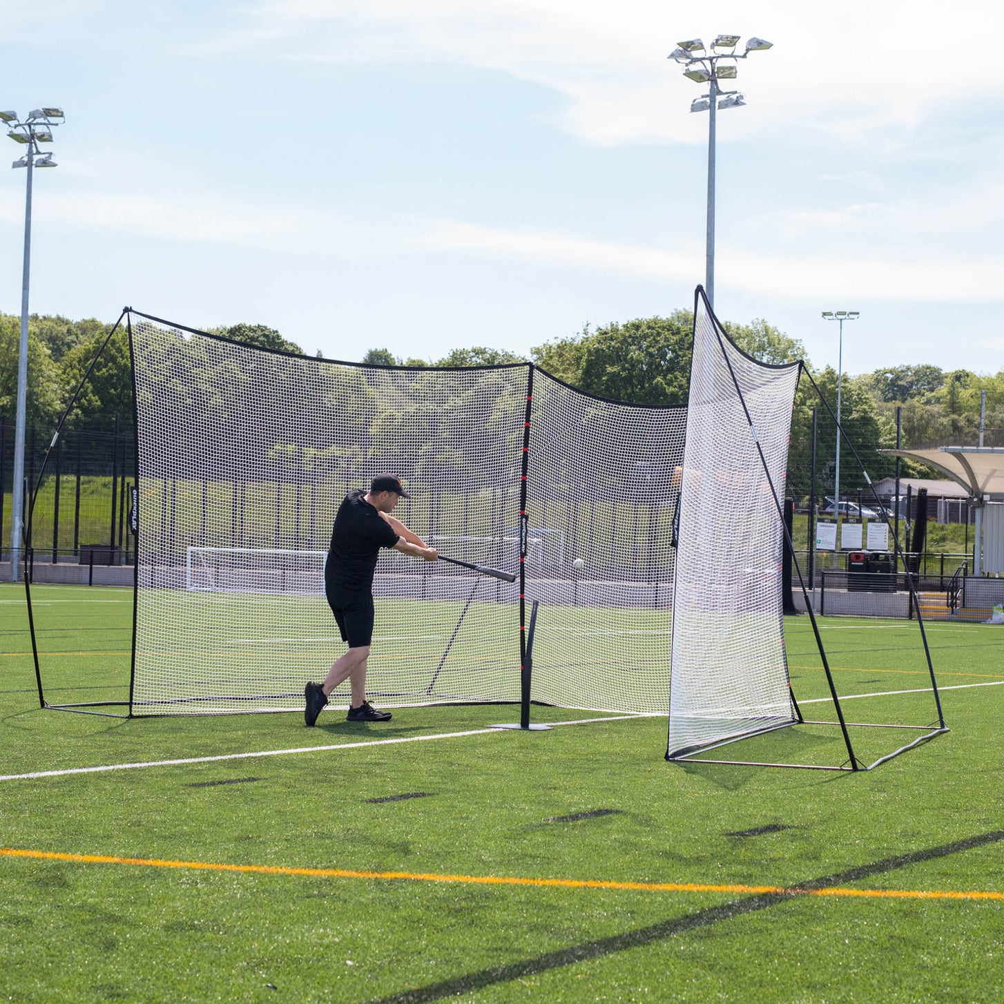 Batter hitting a baseball inside two MEGA NET 12x9' ball-stop nets set at an angle on an artificial pitch.