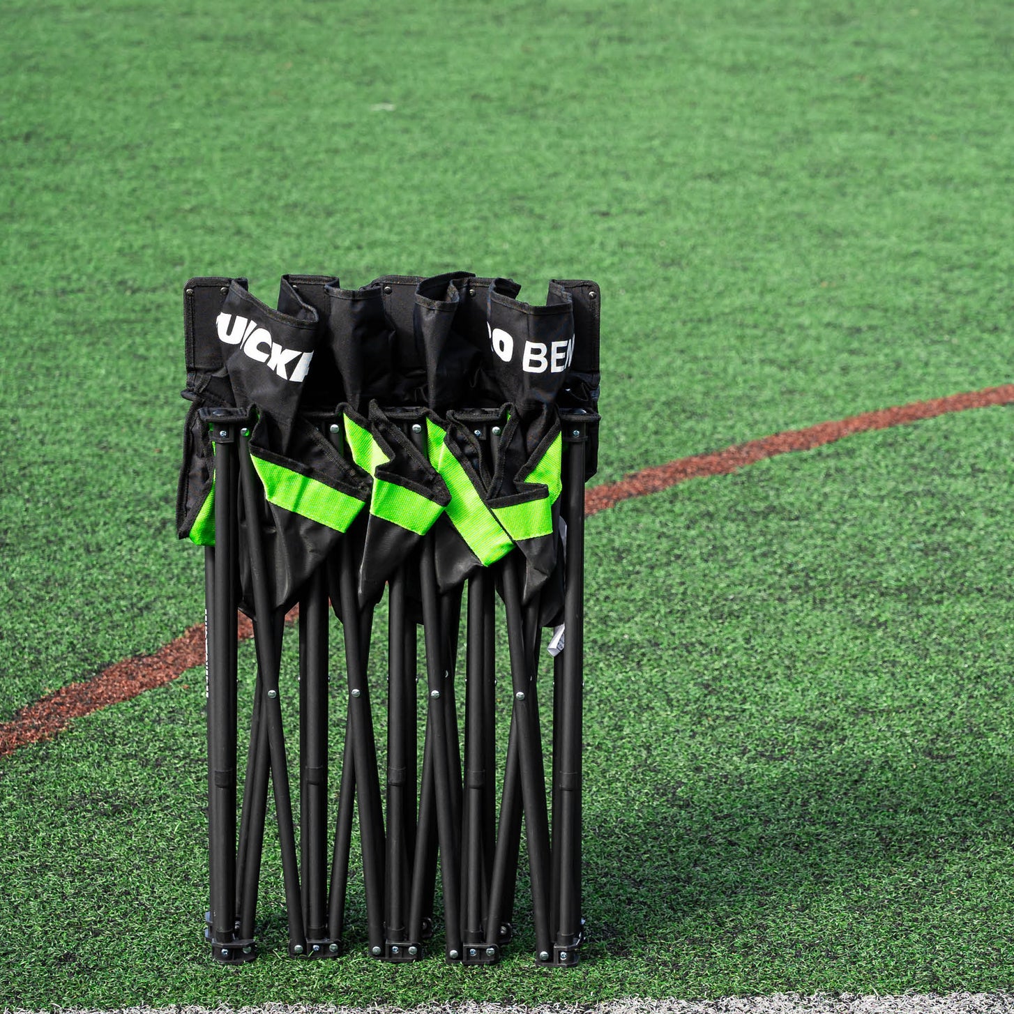 PRO Bench 4 seat subs bench folded and standing upright on an artificial pitch, showing its green webbing.