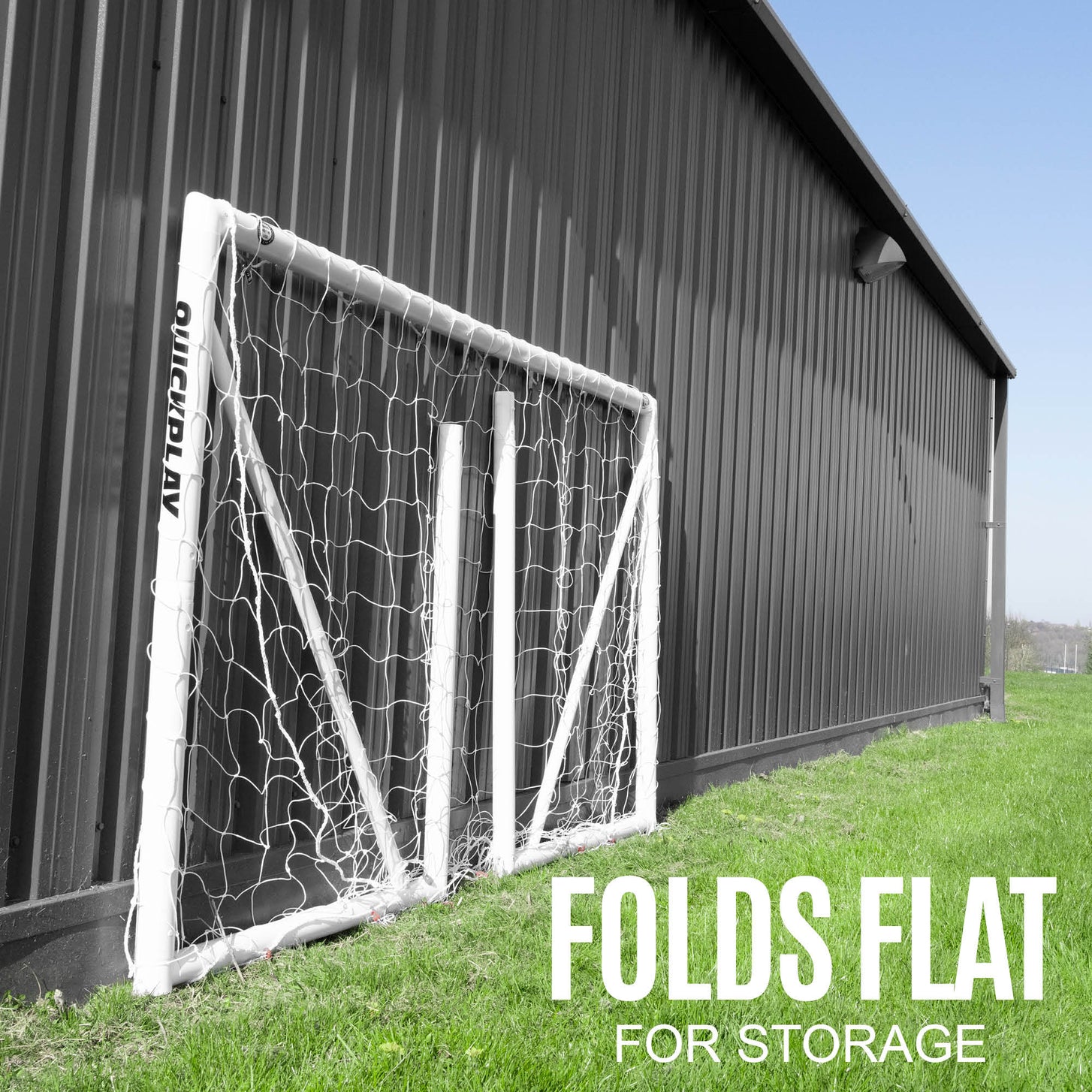 Q-FOLD 8x5' goal folded flat and leaning against a dark metal building on grass, with the text "Folds flat for storage".