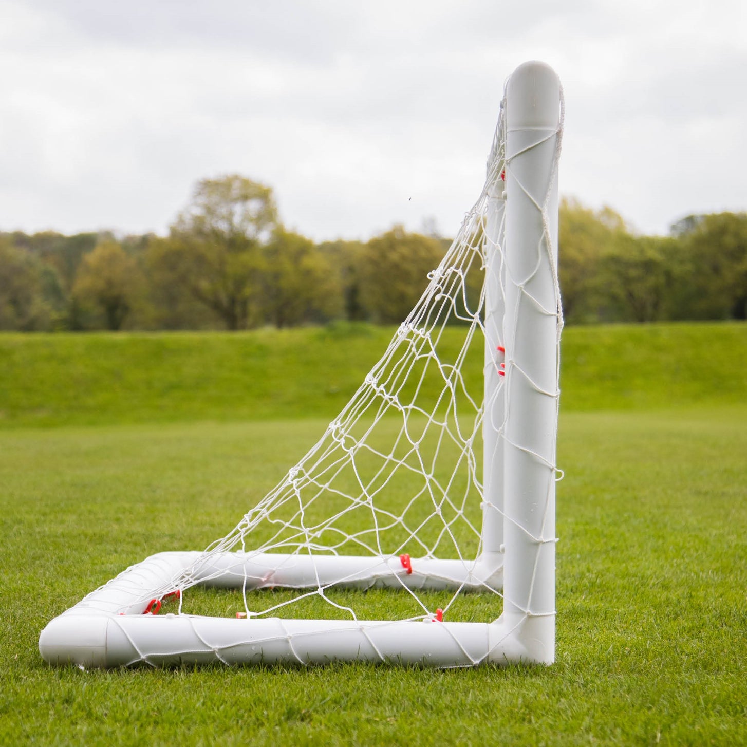 Side view of the Q-FOLD Mini 3x2.5' goal on grass, showing the net running back to the base frame.