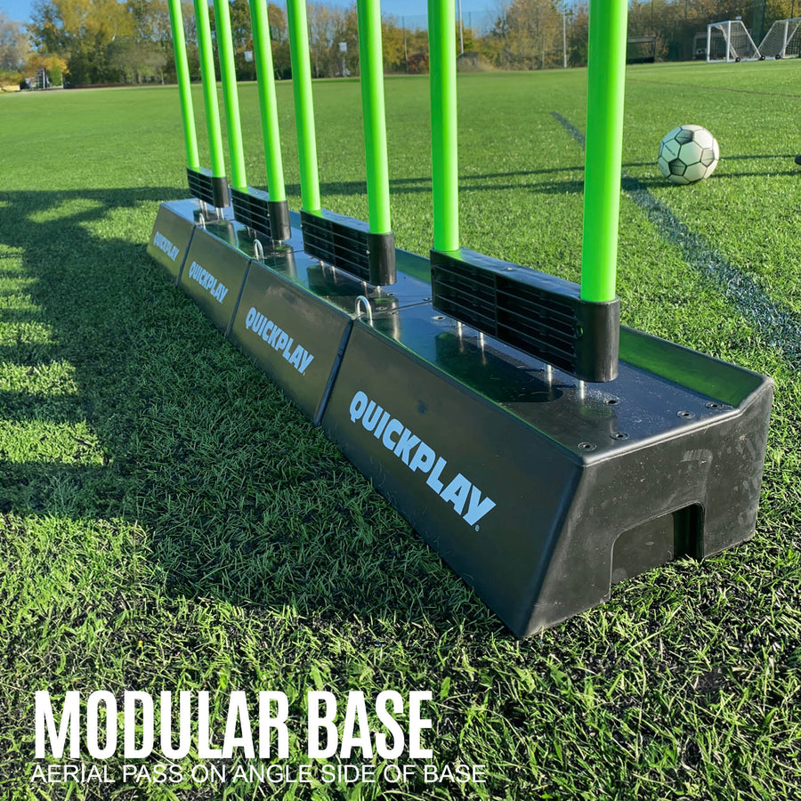Row of joined black QUICKPLAY bases holding green REPLAY Defender poles on grass, with the text "Modular base".