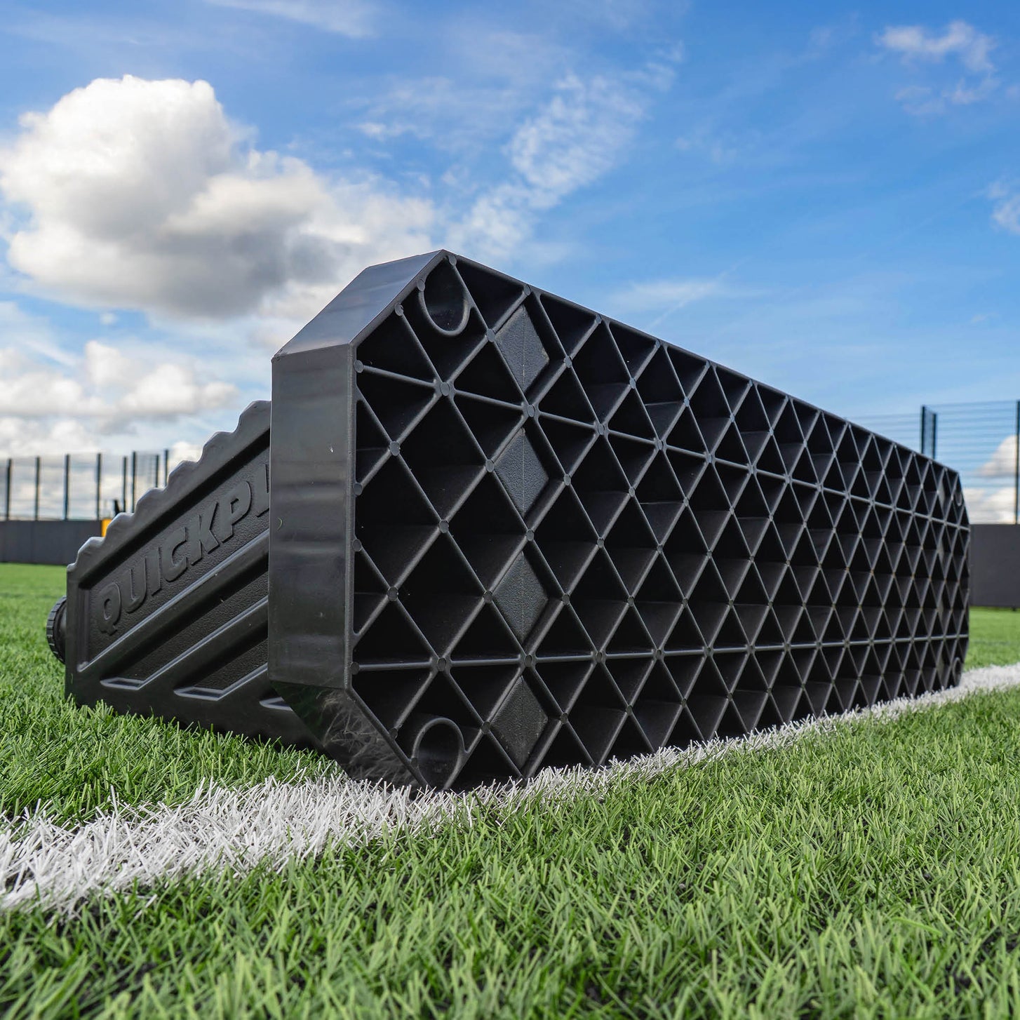 Black plastic REPLAY STATION PLUS rebound board on a grassy field with a blue sky.