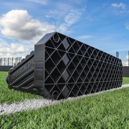 Black plastic REPLAY STATION PLUS rebound board on a grassy field with a blue sky.