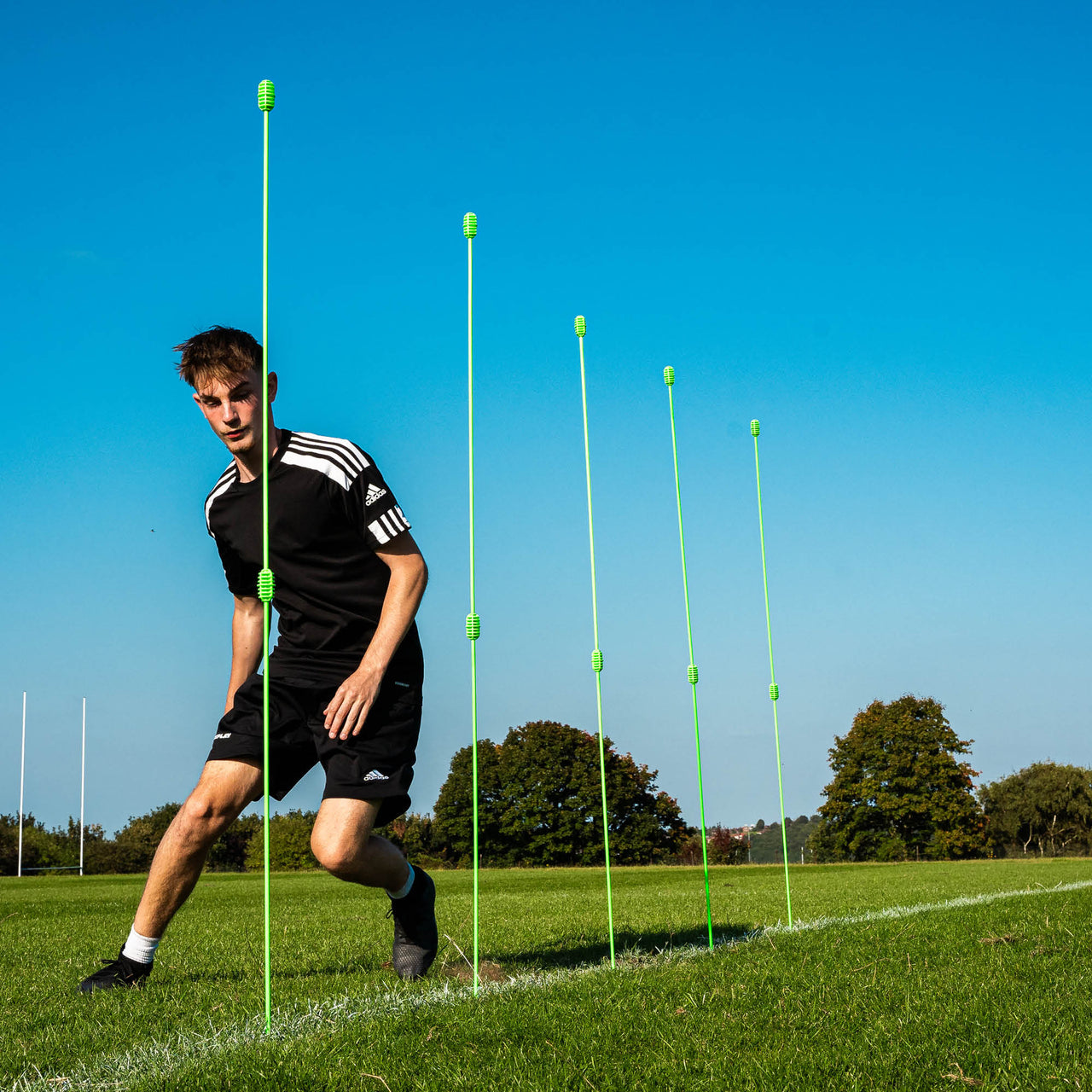 Person on a football pitch with green training poles against a blue sky