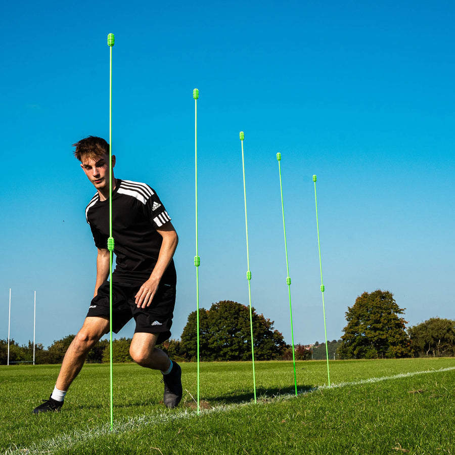 Person on a football pitch with green training poles against a blue sky