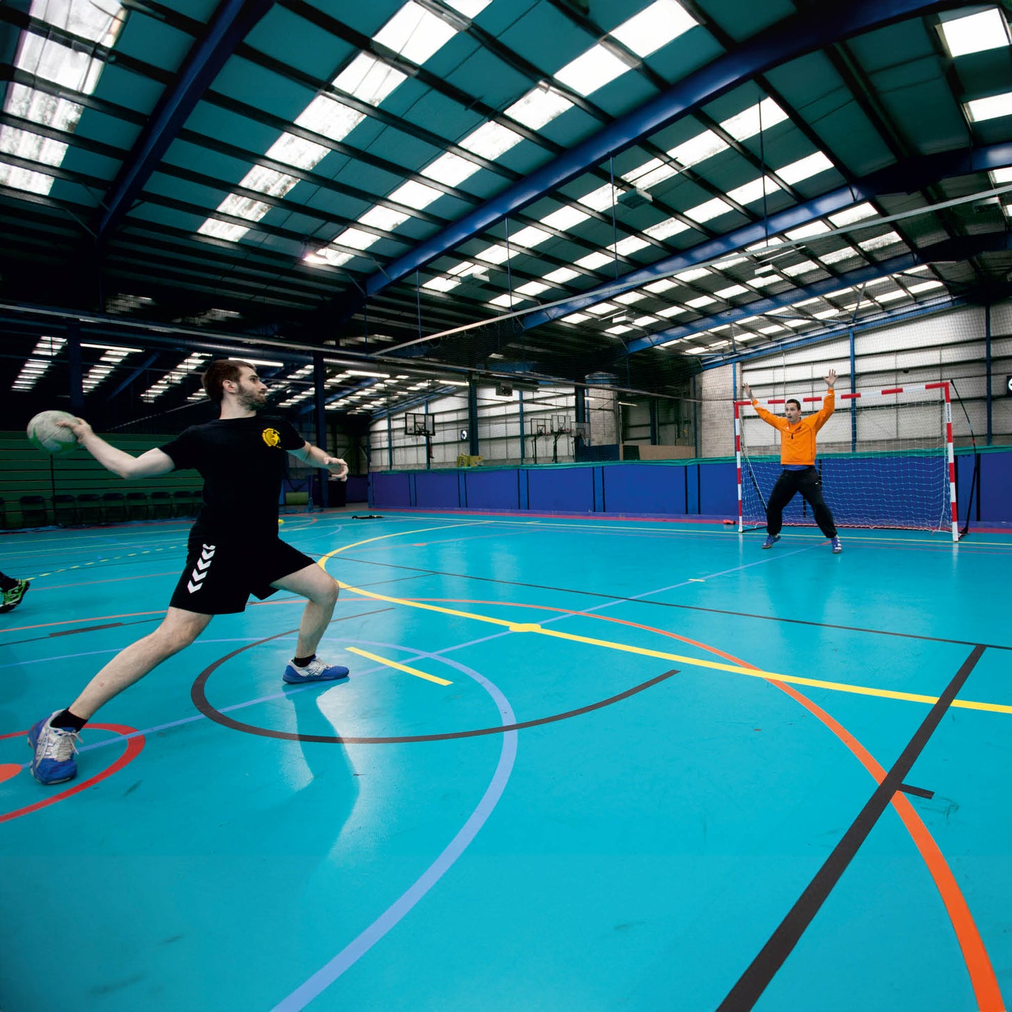 Portable Handball Goal Adult 3x2m listing: a player throwing towards a goalkeeper at a red and white goal in a blue sports hall.