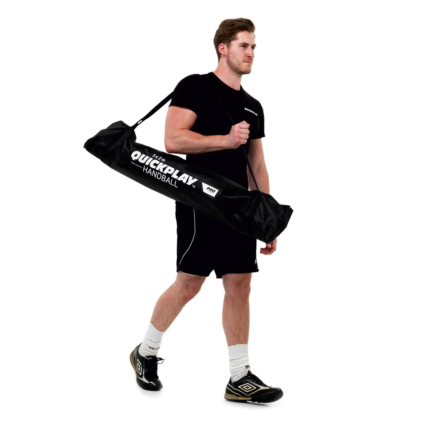 Man carrying the Portable Handball Goal Adult 3x2m in its black QUICKPLAY handball bag on a white background.