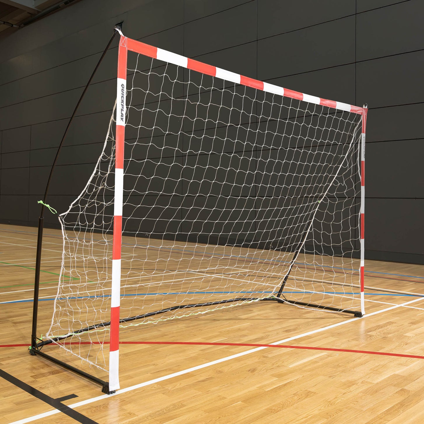 Portable Handball Goal Adult 3x2m with a red and white frame, seen from the side on a wooden sports hall floor.