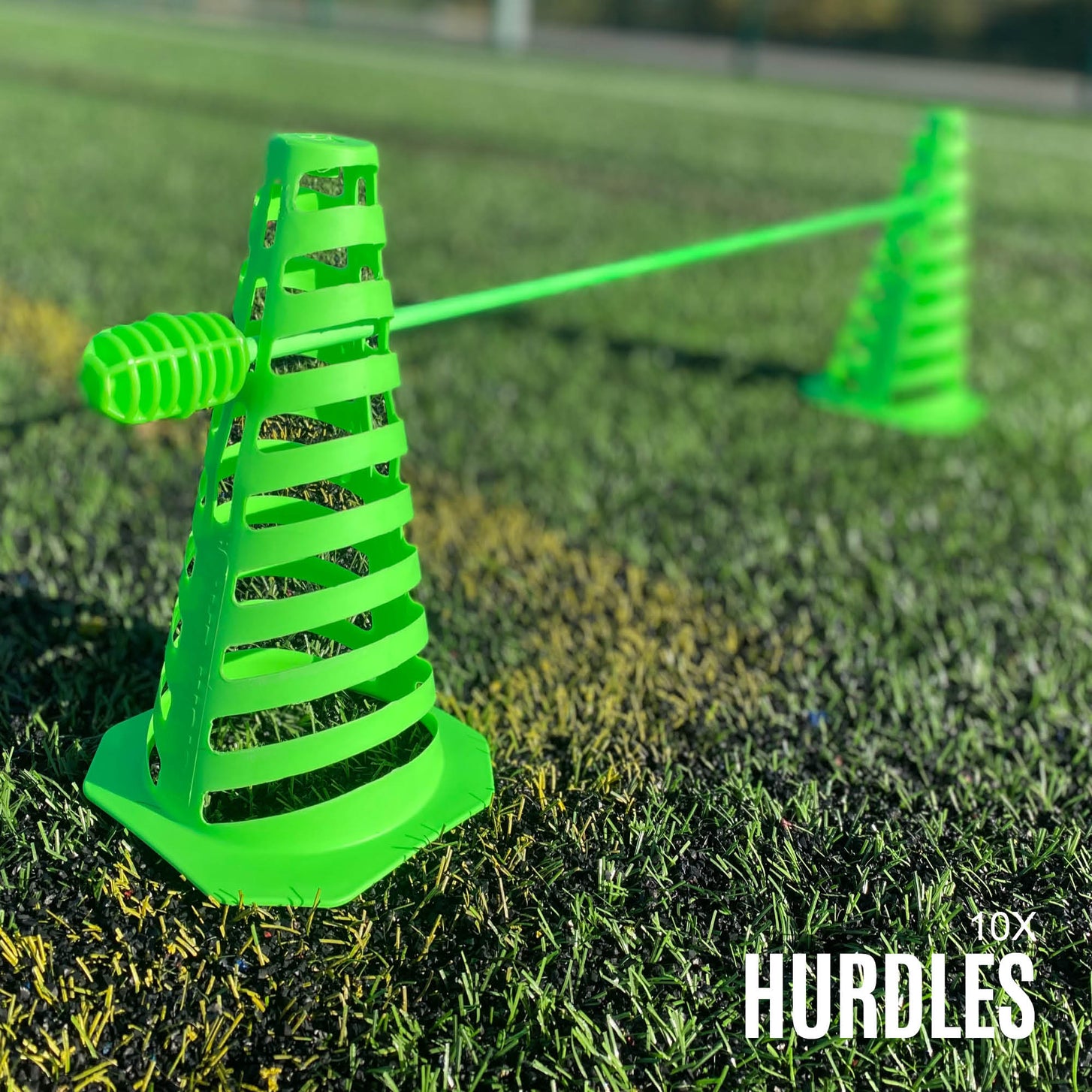Close-up of a green slotted cone holding a green pole as a low hurdle on artificial grass, with the text "10x hurdles".