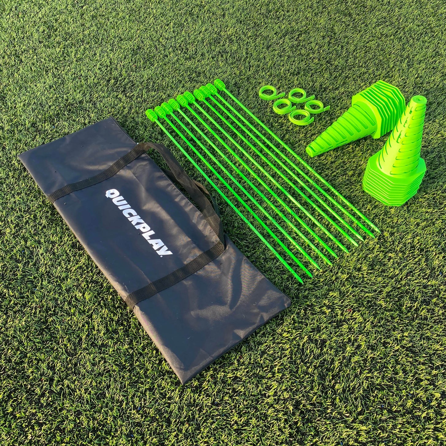 PRO Speed & Agility Set laid out on artificial grass: a black QUICKPLAY bag, green poles, green rings and two stacks of slotted cones.