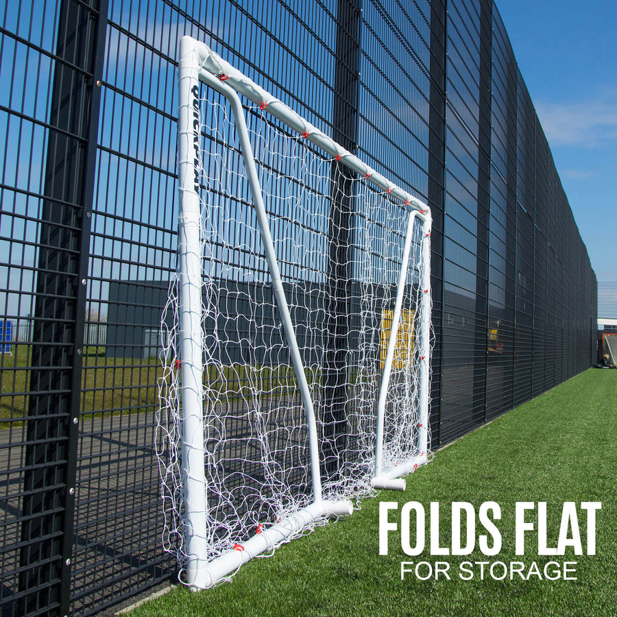 Q-FOLD Match 12x6' goal folded flat beside a black fence on artificial grass, with the text "Folds flat for storage".