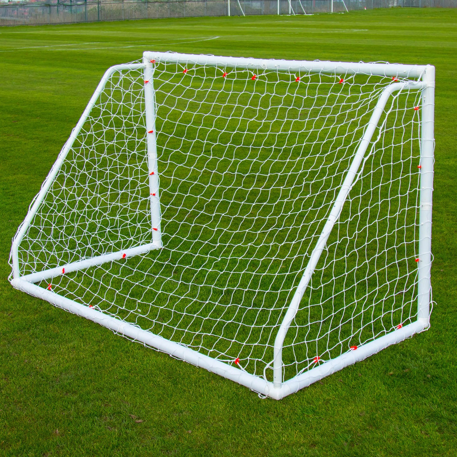 Q-FOLD Match 8x5' goal seen from behind on a grass pitch, showing the white frame, net and red net clips.