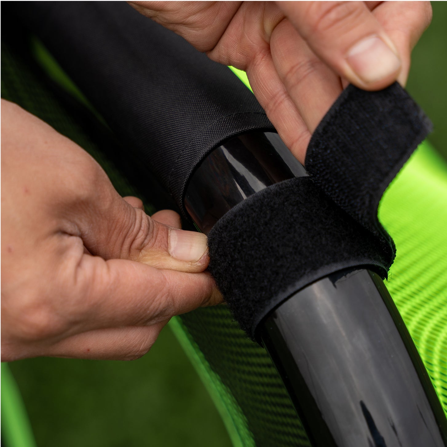 Close up of hands fastening a black hook and loop strap of the PRO ALU Training Target Net Lite 6x4' around a goal post.