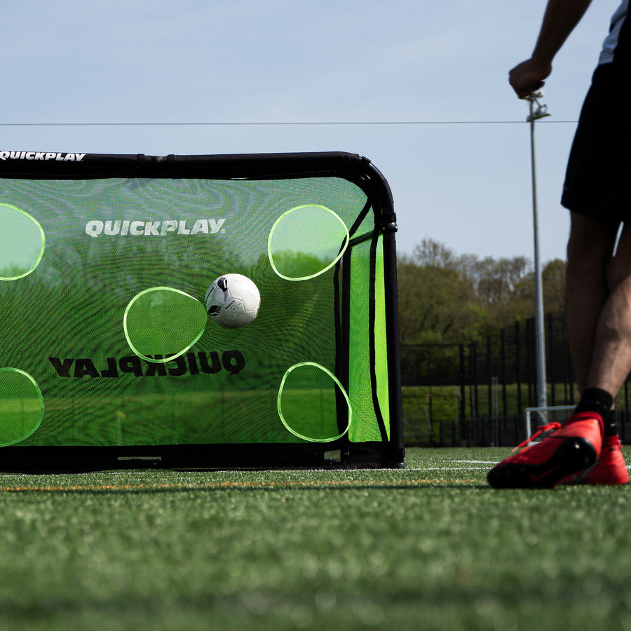 Ball flying at a target hole in the PRO ALU Training Target Net Lite 6x4', with a player in red boots beside the goal.