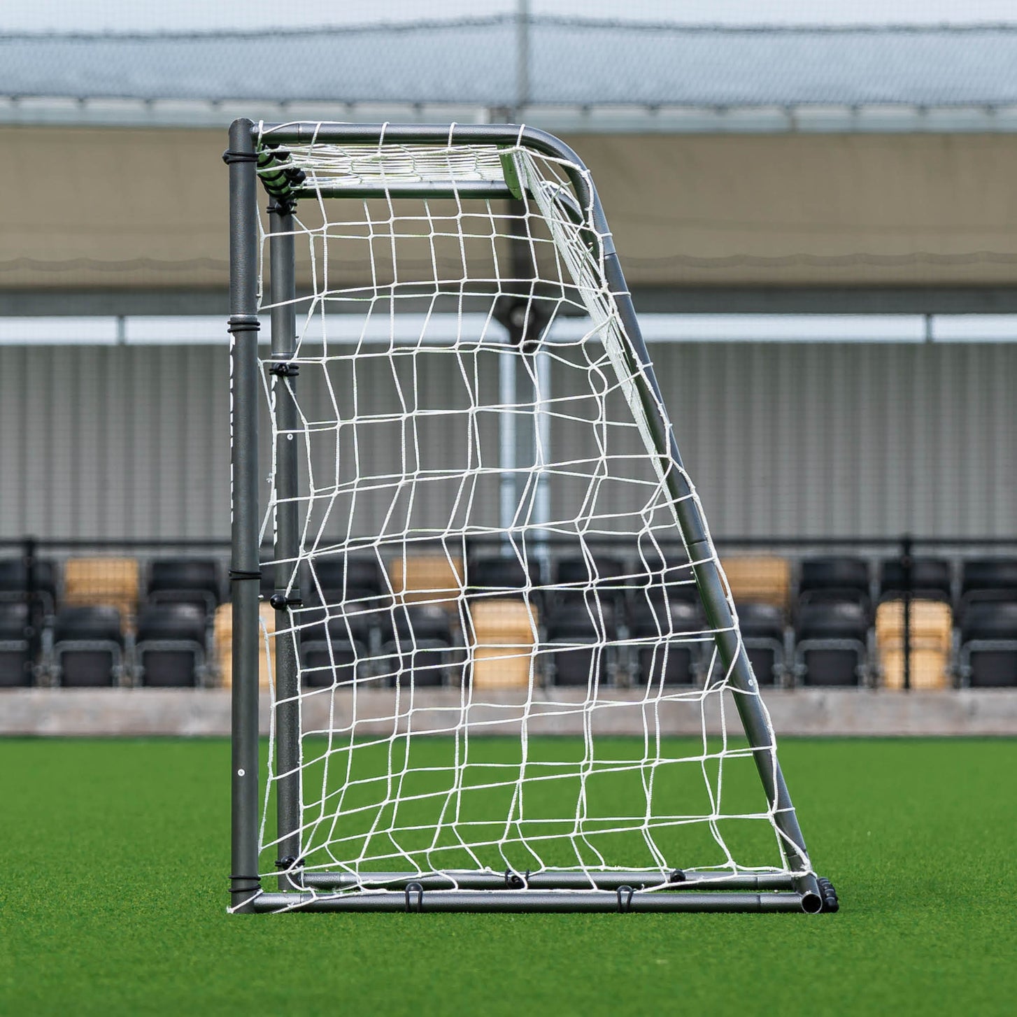 GS Series Football Goal 6x4' side view showing the frame depth and net, in front of a stadium stand.