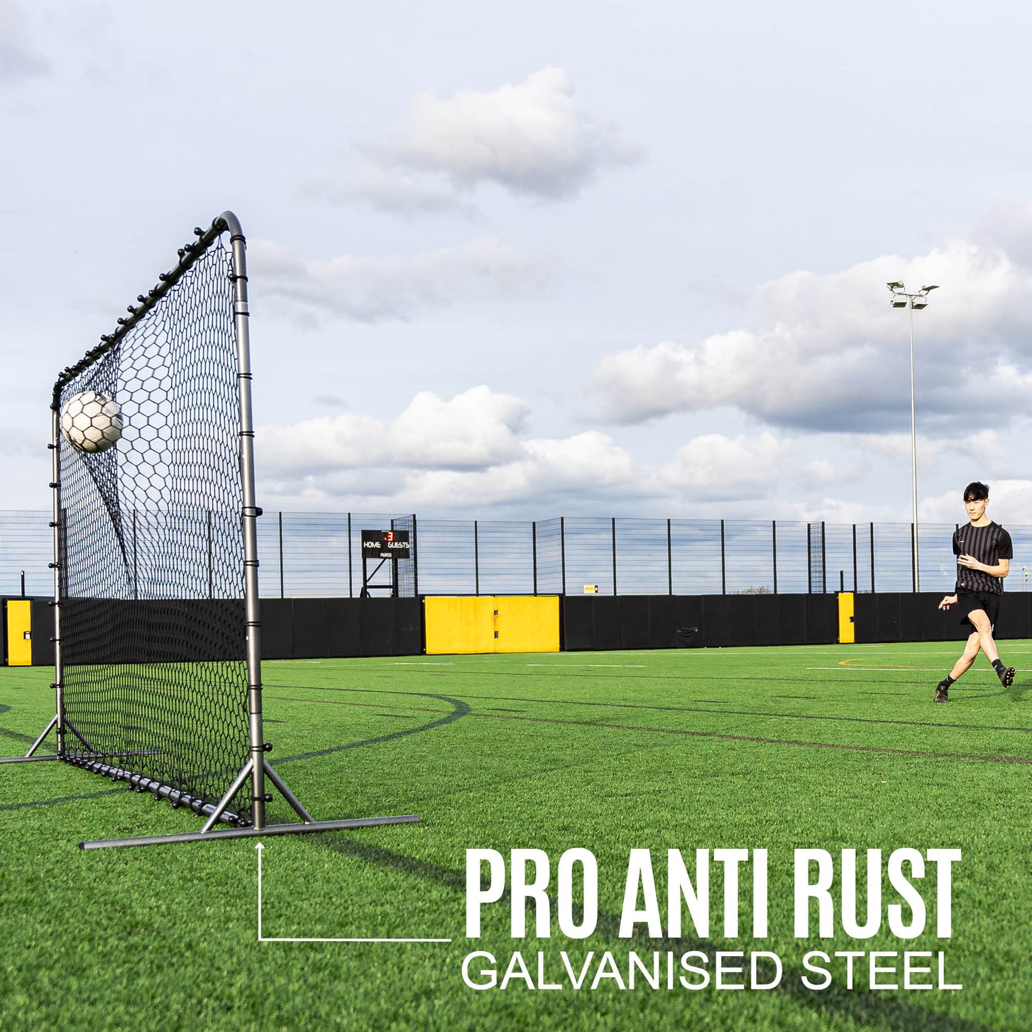 Player passing a ball into the Barrier Net & Rebounder 12x6' on an artificial pitch, with the text "Pro anti rust galvanised steel".
