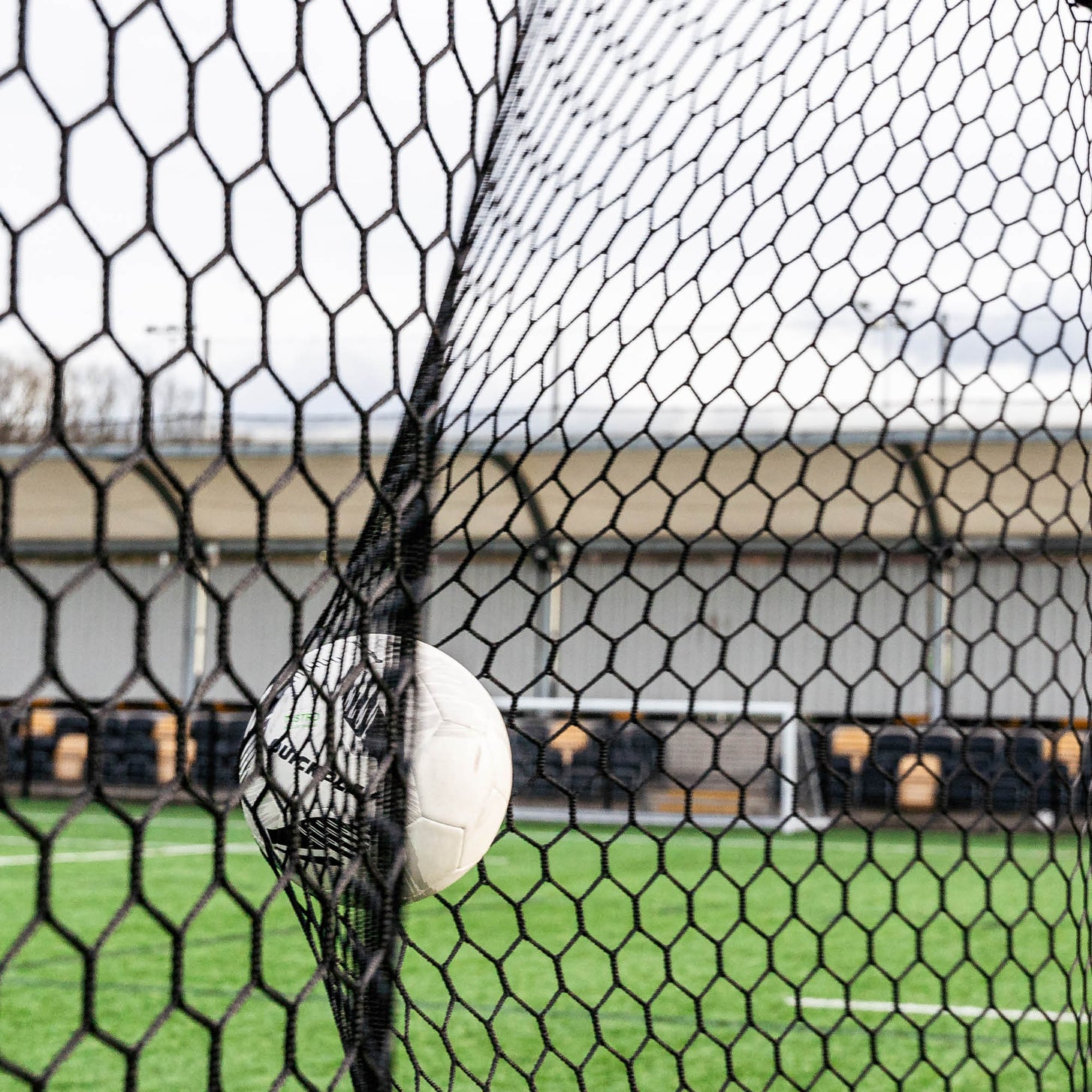 Close up of a ball pushing into the black hexagonal net of the Barrier Net & Rebounder 12x6'.