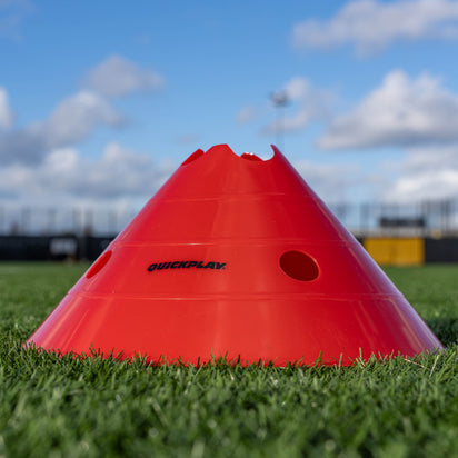 Red plastic cone with 'Quickplay' branding on grass, blue sky background