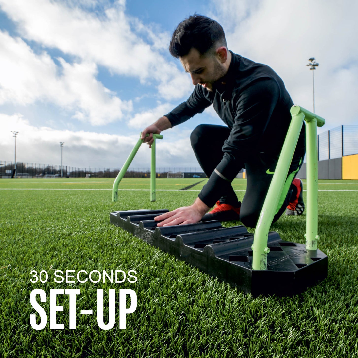 Man kneeling on artificial grass fitting the green frame to the REPLAY Station board, with set-up text.