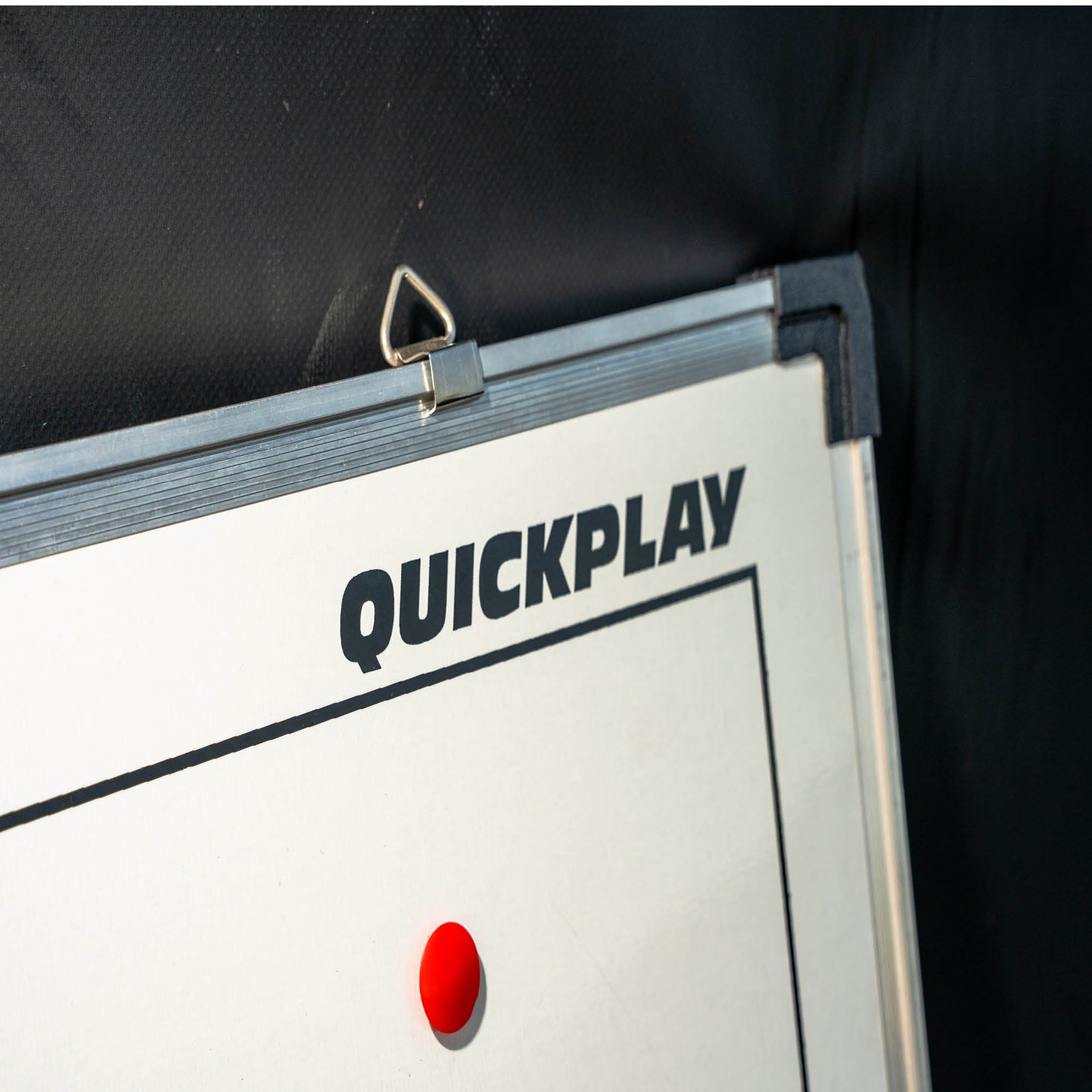 Magnetic Whiteboard (S) 30x45cm top corner with hanging loop and QUICKPLAY logo, against a dark wall.
